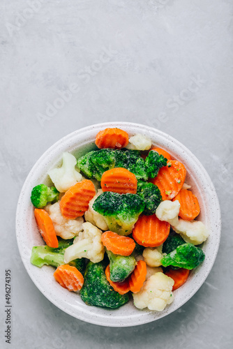 Frozen vegetables. Frozen carrots, broccoli and cauliflower in bowl on gray stone background