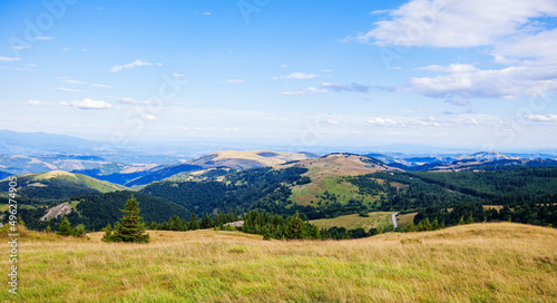 Beautiful nature panoramic view of mountain range. Peaceful landscape. Green hills and fields on summer day. Blue sky with clouds. Panorama of Kopaonik mountain. Serbia. Europe.