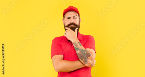 Fényképezés Pensive man in casual red cap and tshirt stroking chin yellow background, volunt