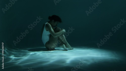Woman sinking on gound of swimming pool hugging knees photo