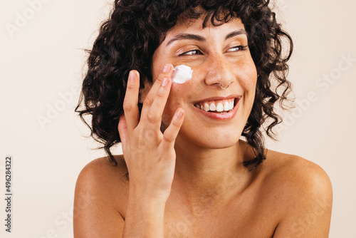 Happy young woman applying moisturizing cream on her face