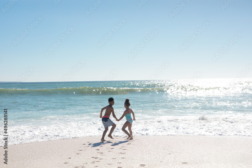 Full length of african american brother and sister holding hands while playing at beach on sunny day