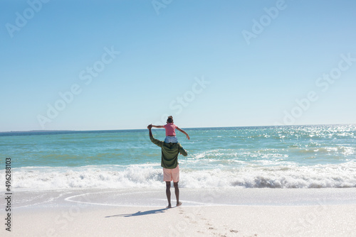 African american girl enjoying sunny day on father's shoulders standing at beach, copy space