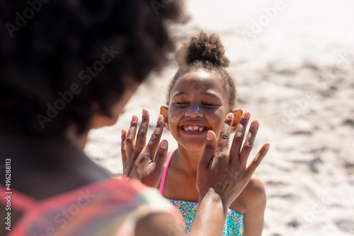Fotografia Cheerful african american girl smiling with eyes closed while mother applying su