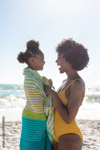 Side view of cheerful african american mother and daughter at beach against clear sky on sunny day