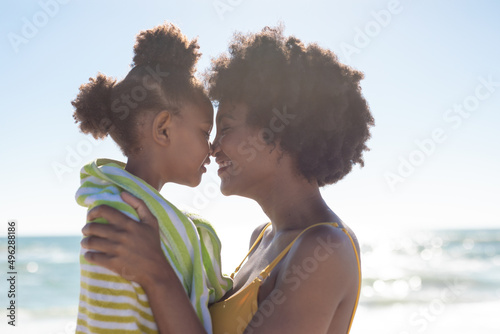 Side view of happy african american mother and daughter rubbing noses together at beach