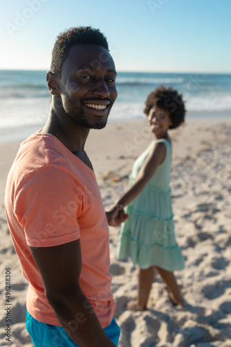 Portrait of smiling african american man holding hand with girlfriend at beach on sunny day