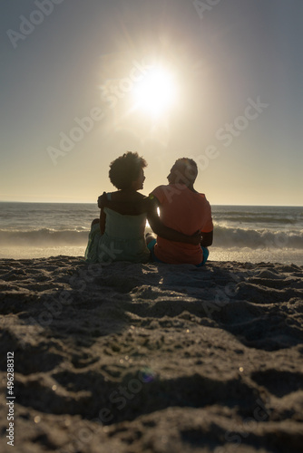 Surface level view of happy african american couple sitting with arms around on sand at beach