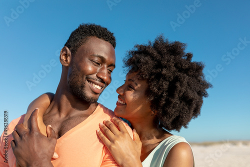Romantic african american couple looking at each other against blue sky on sunny day