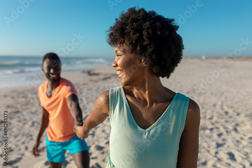 Smiling african american woman looking over shoulder while leading boyfriend at beach on sunny day © wavebreak3