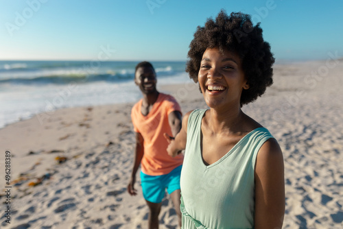 Portrait of cheerful african american woman holding hand with boyfriend while leading at beach
