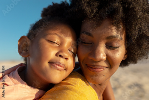 Close-up of african american girl with eyes closed relaxing on mother's shoulder at beach