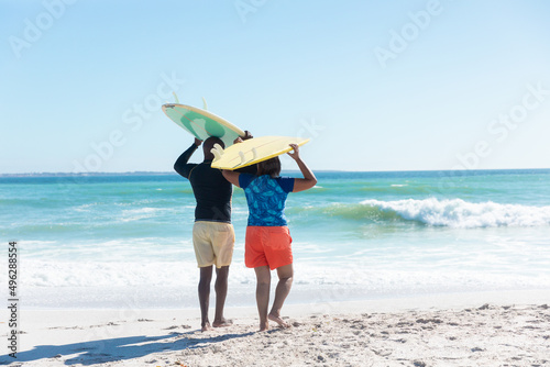 African american senior couple carrying surfboards on heads at beach against sky with copy space