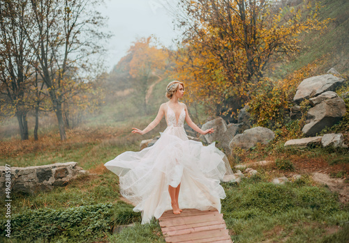 Fantasy woman elf in white creative design vintage dress walks in autumn nature, yellow foliage trees, green dress, deep dence fog. Silk fabric wave fly flutter in motion. Girl princess fashion model.