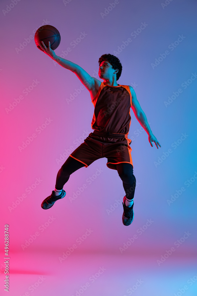 Obraz premium Young energetic man playing basketball isolated on gradient pink blue studio background in neon light. Youth, hobby, motion, activity, sport concepts.