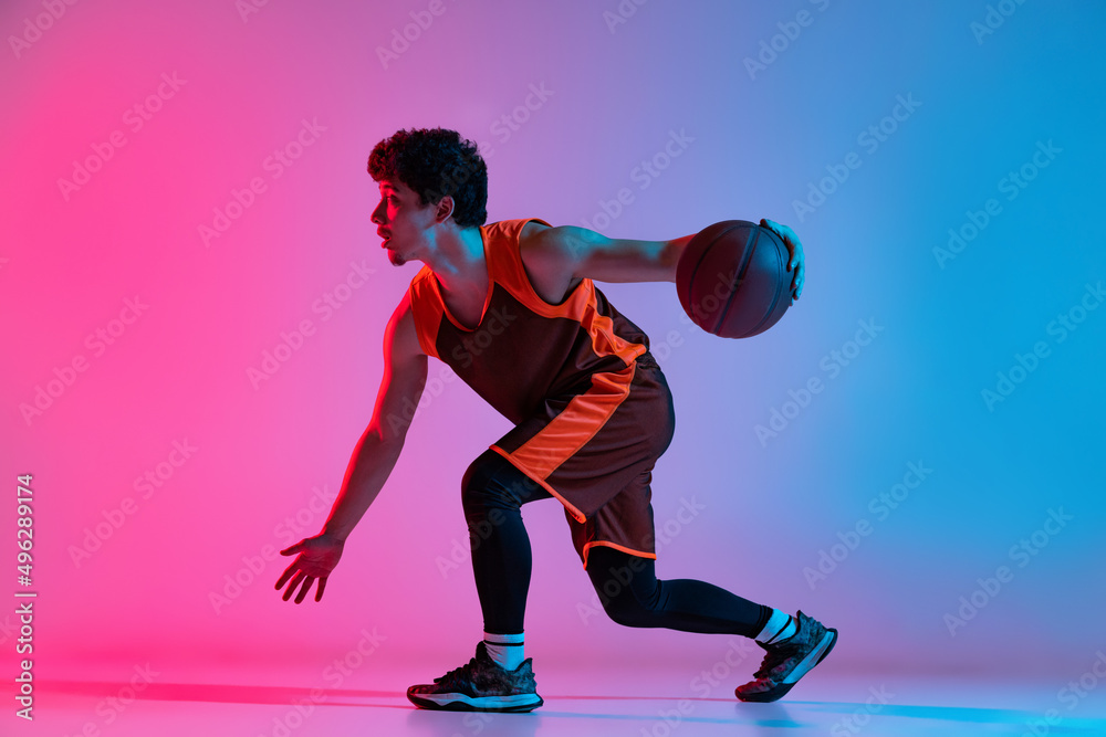Sportive man playing basketball isolated on gradient pink blue studio background in neon light. Youth, hobby, motion, activity, sport concepts. Sportive man playing basketball isolated on gradient pink blue studio background in neon light. Youth, hobby, motion, activity, sport concepts.