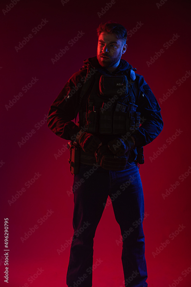airsoft player in full gear with guns GG RK74. a man in headphones, body armor, with a backpack and a belt. red background. colored, blue-red light