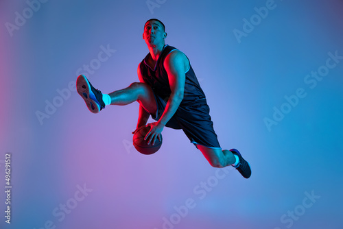 Young sportive man playing basketball isolated on blue studio background in neon light. Youth, hobby, motion, activity, sport concepts.