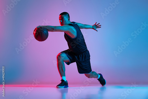 Young sportive man, basketball player training with ball isolated on blue studio background in neon light. Youth, hobby, motion, activity, sport concepts. © master1305