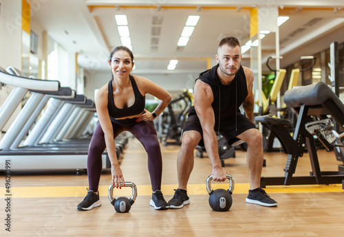 Athletic man and woman training together with kettlebells in modern gym