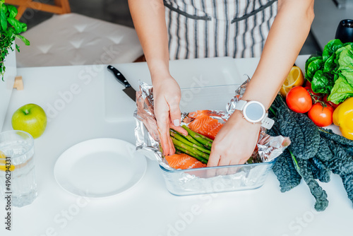 Baked salmon with green asparagus recipe steps. Step two. Woman putting sliced fresh salmon into the foiled baking form. Step by step recipe. Healthy cooking at home in kitchen according to recipe