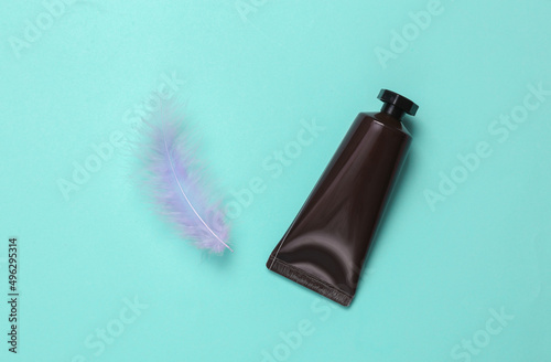 tube of cream with a feather on turquoise background. Beauty concept. Flat lay