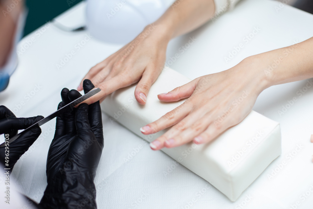 Obraz premium Manicurist files with nail file the nails of hands of woman client in nail salon