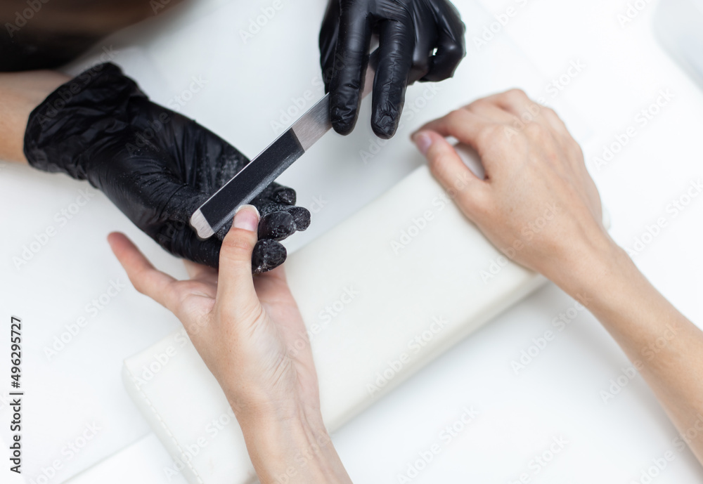 Manicurist files with nail file the nails of hands of woman client in nail salon