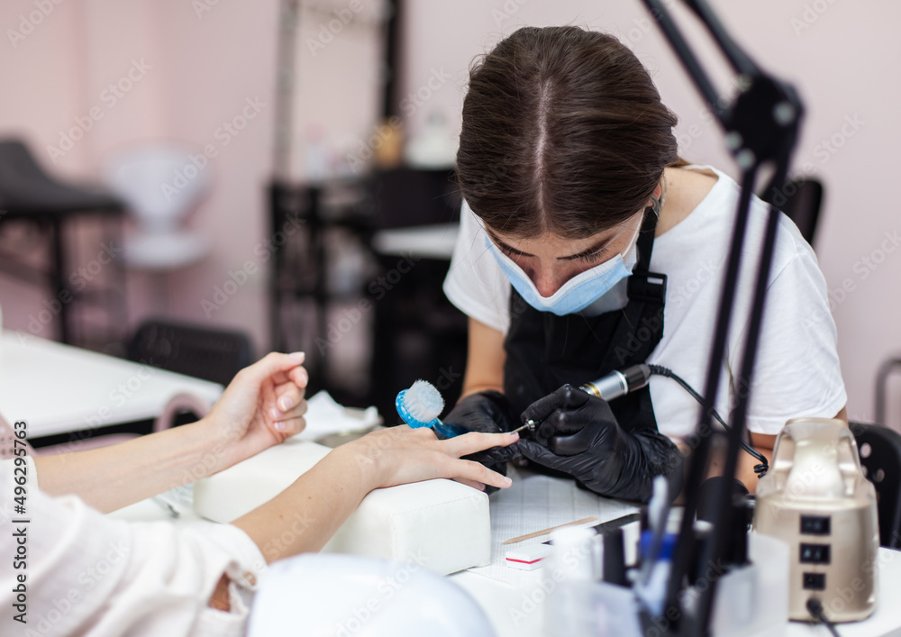 Manicure master removes cuticles with electric file machine on female hand in nail salon Manicure master removes cuticles with electric file machine on female hand in nail salon