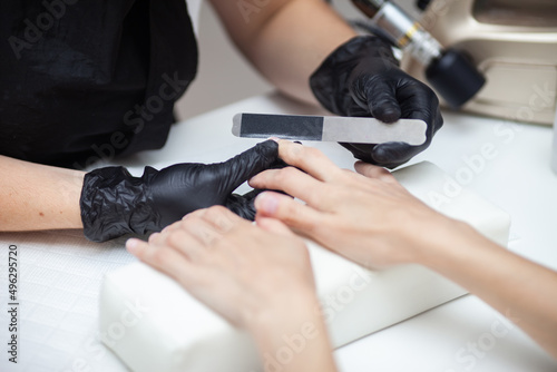 Manicurist files with nail file the nails of hands of woman client in nail salon