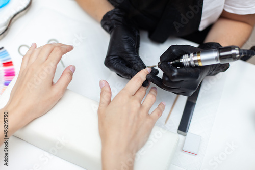 Manicure master removes cuticles with electric file machine on female hand in nail salon