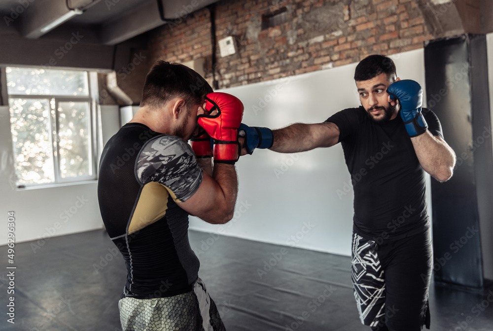 Two sparring partners of a kickboxer in boxing gloves practice kicks in a sports hall Two sparring partners of a kickboxer in boxing gloves practice kicks in a sports hall