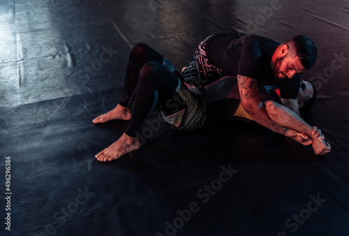 Two athletic male fighters are training, practicing a painful hold in a sports hall. DArk neon light