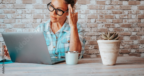 Businesswoman thinking on front of laptop at the desk with bricks background. Modern people working with computer. Online job business activity. Attractive thoughtful lady in smart working at home photo