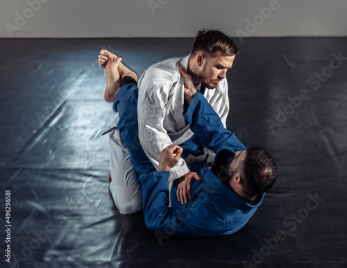 Two fighters sparring a partner in a kimono are training painful holds in a sports hall