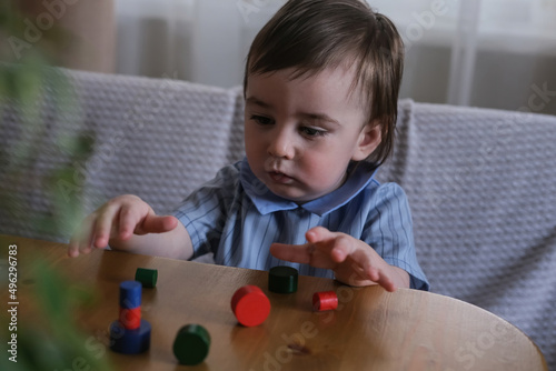 A one-year-old child plays with multi-colored wooden figurines. Development of fine motor skills and logical thinking of kids