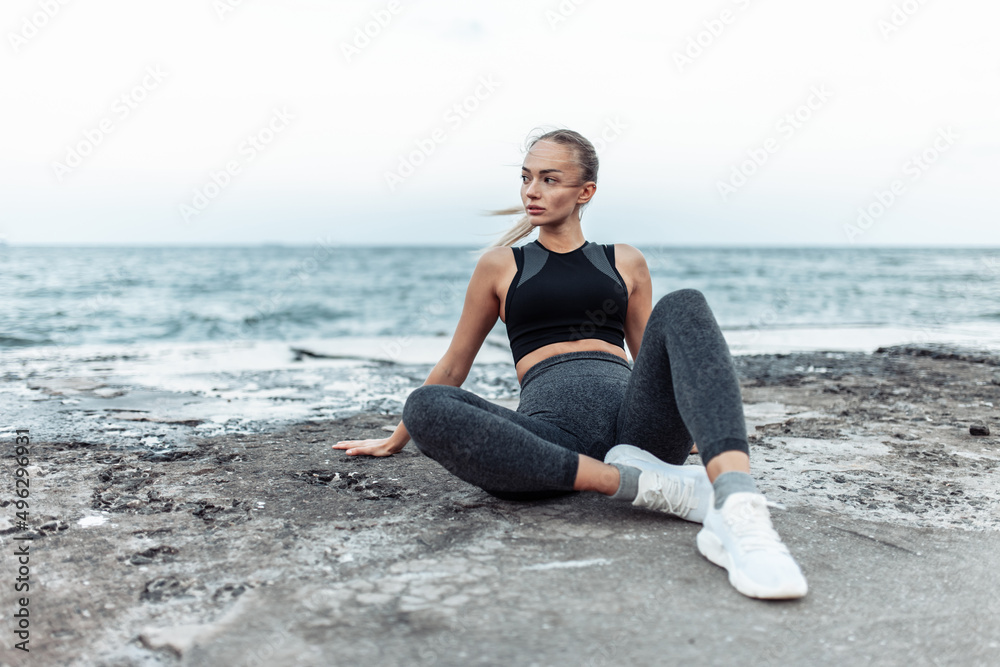 Fit woman in sportswear sitting on urban beach Fit woman in sportswear sitting on urban beach