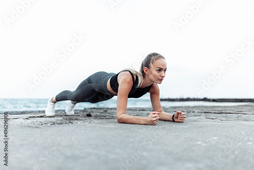Beautiful young fit woman in sportswear doing olank exercise alone on urban beach. Healthy lifestyle concept