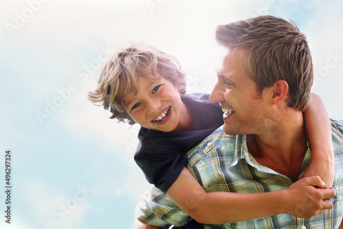 Foto Playful father giving his son piggy back ride against sky