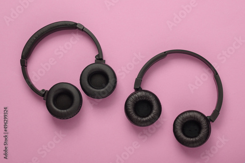 Two pairs of black wireless stereo headphones on pink background