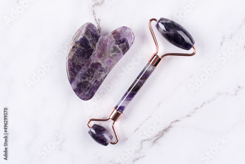 Facial massage kit - amethyst gua sha tool and face roller on white marble background. Face roller, massager made from natural stones, home spa concept photo