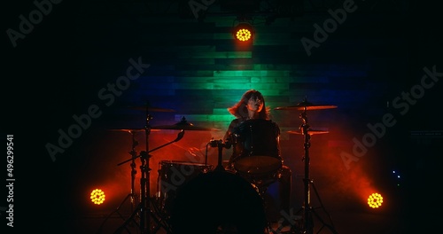 Female drummer with red hair playing on stage during rock show in nightclub