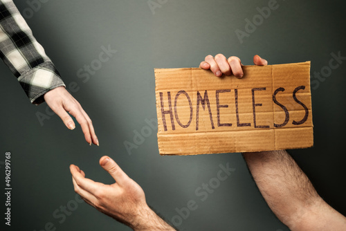 Tableau sur toile A woman extends a helping hand to a man holding a cardboard box with the text homeless