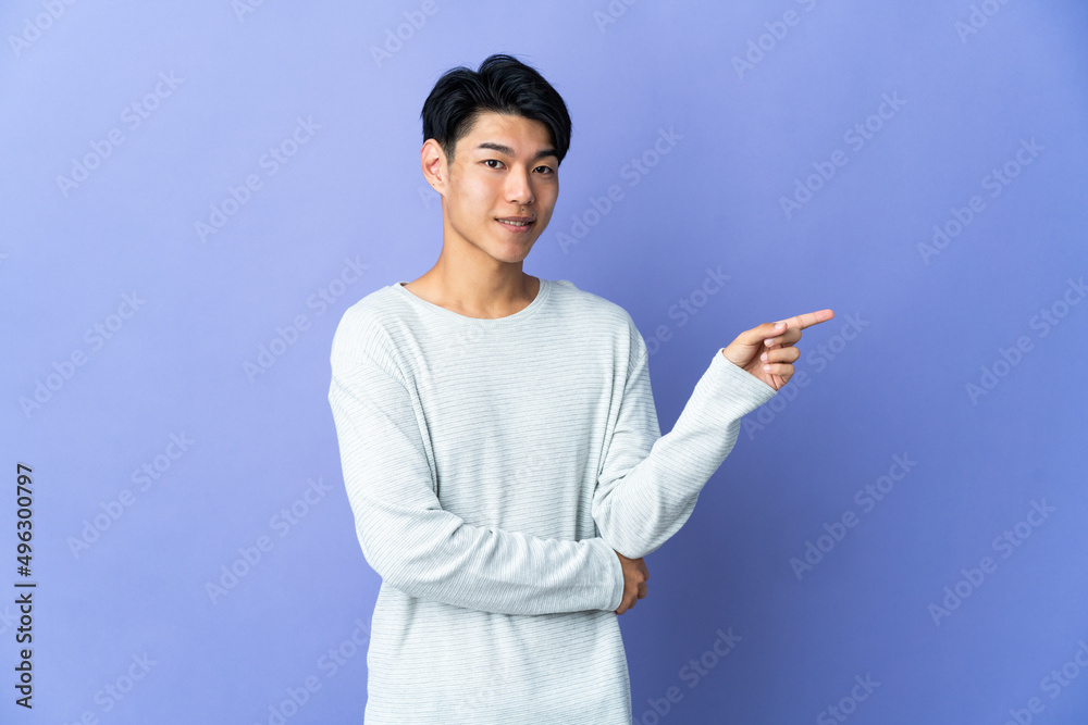 Young Chinese man isolated on purple background pointing finger to the side Young Chinese man isolated on purple background pointing finger to the side
