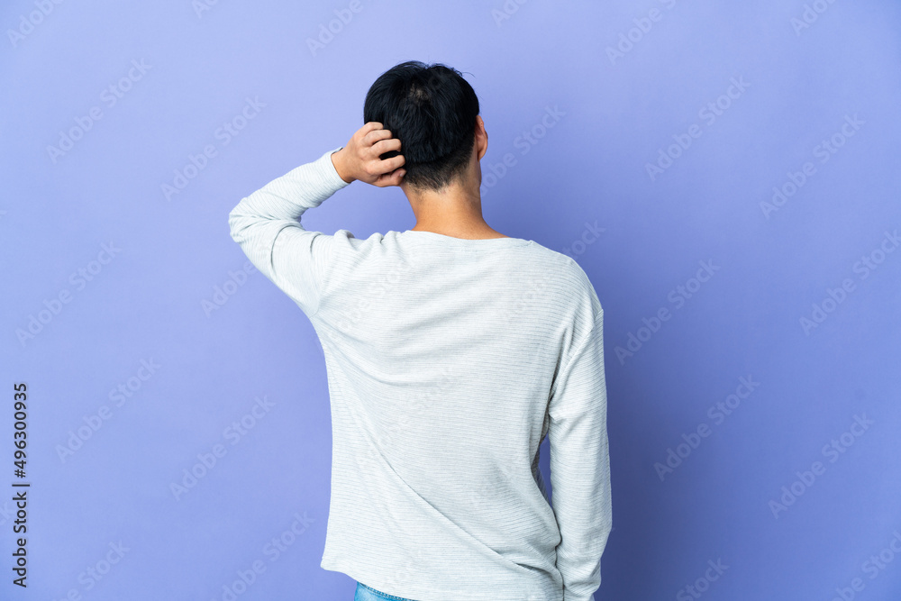 Young Chinese man isolated on purple background in back position and thinking Young Chinese man isolated on purple background in back position and thinking
