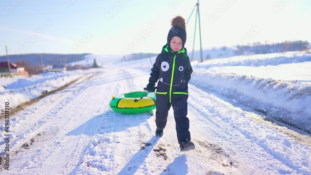 Little boy tubing snowy downhill, family time. Happy kid having fun outdoors in winter on sledge. Active boy sliding together down the hill on snow tube.
