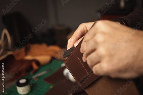tanner makes genuine leather wallet, professional craftsman, closeup, indoor, authentic, business. Handiwork. treats edges with sandpaper
