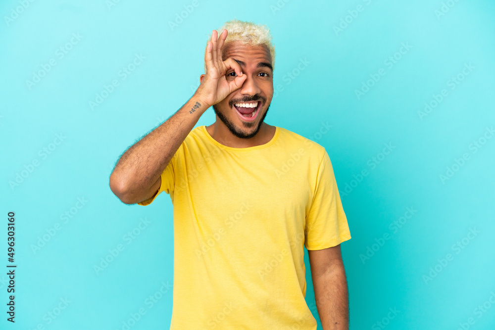 Young Colombian handsome man isolated on blue background showing ok sign with fingers Young Colombian handsome man isolated on blue background showing ok sign with fingers