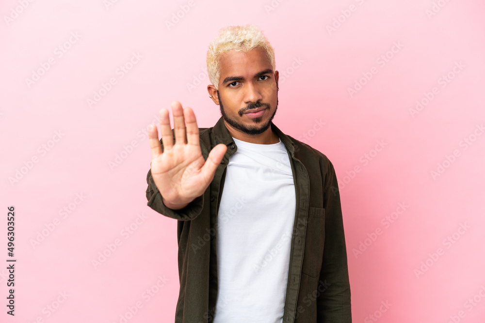 Young Colombian handsome man isolated on pink background making stop gesture
