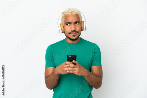 Young Colombian handsome man isolated on white background listening music with a mobile and thinking © luismolinero